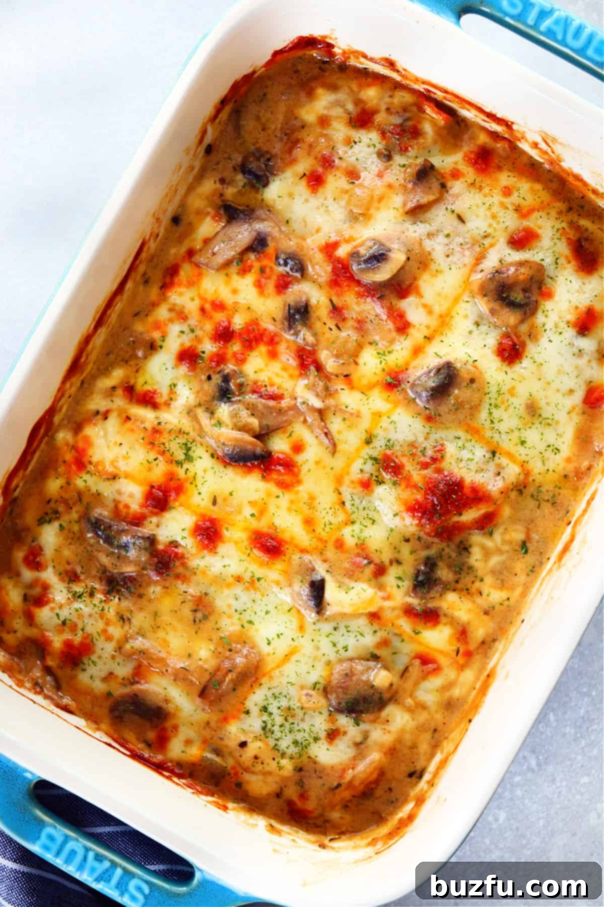 Chicken casserole with mushroom sauce and melted cheese in a blue Staub baking dish.