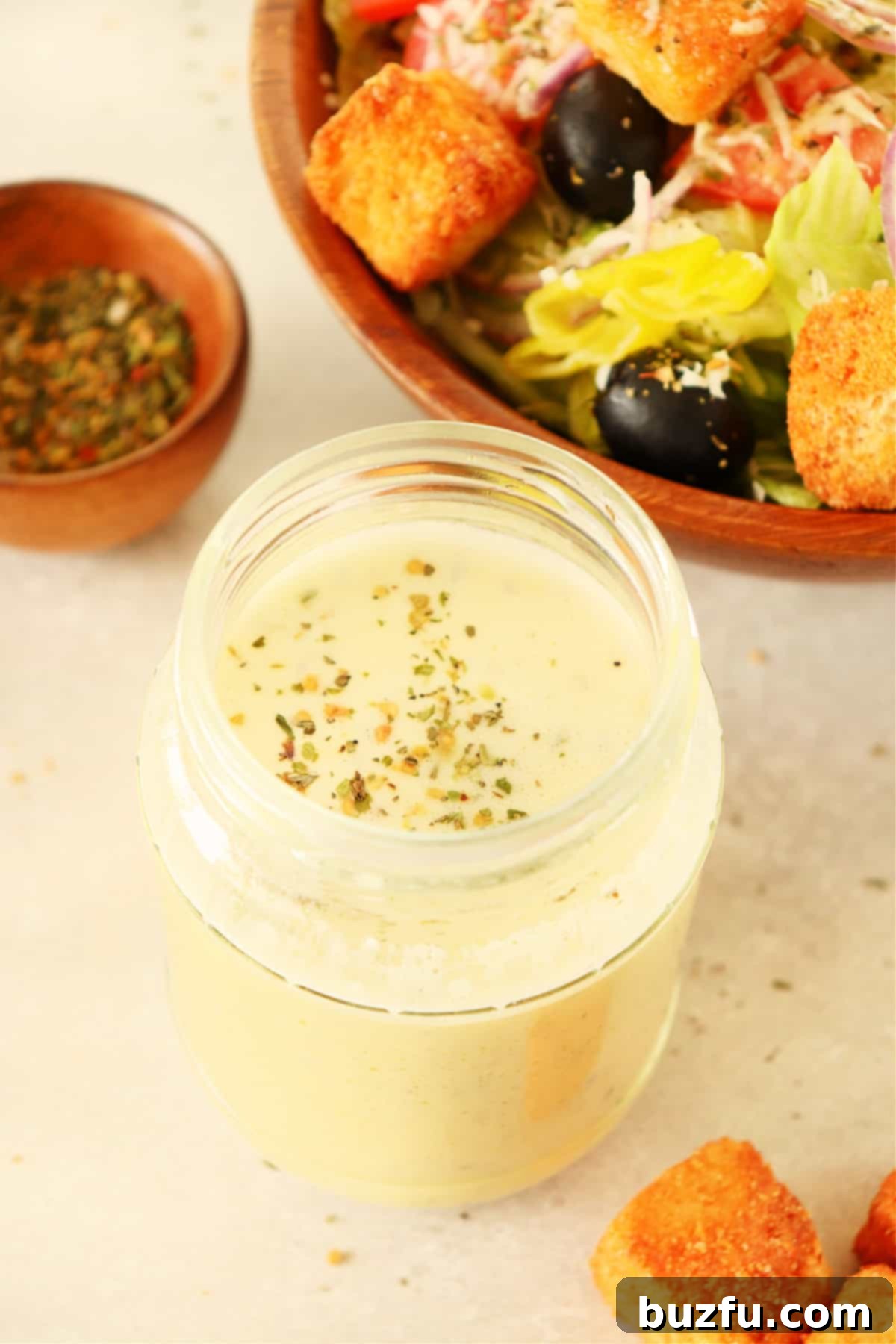 No-Fuss Salad Dressings 8 Creamy dressing in a glass jar next to a bowl with salad.