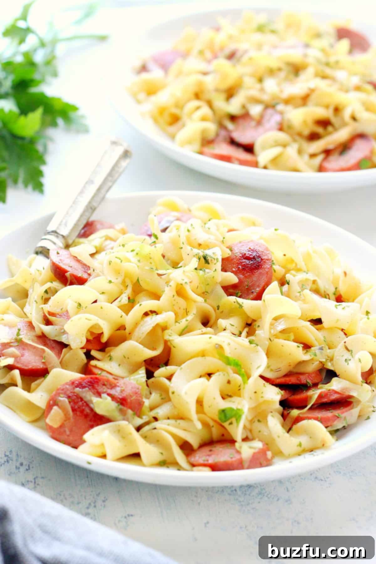 Weekly Meal Plan 3 3 A serving of golden-brown cabbage and noodles with slices of savory sausage on a pristine white plate, garnished with fresh herbs, ready to be enjoyed.