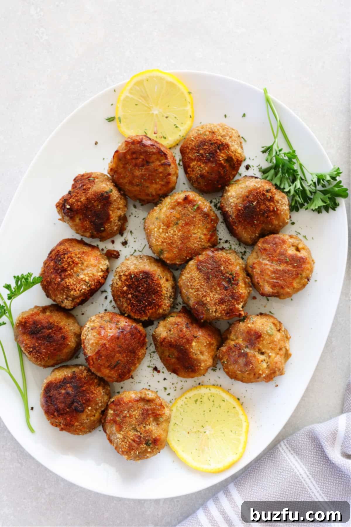 Weekly Meal Plan 3 6 Succulent, oven-baked turkey meatballs arranged on a white oval platter, garnished with vibrant green herbs and fresh lemon slices, ready for serving.