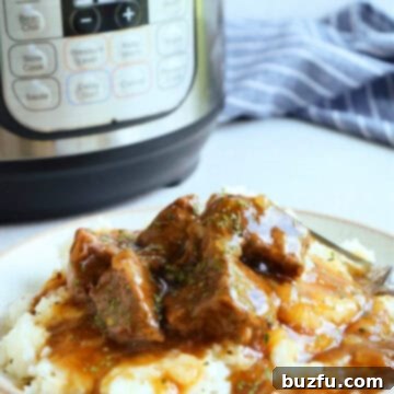 Side photo of beef tips with gravy on mashed potatoes. on a plate, with the Instant Pot in the background.