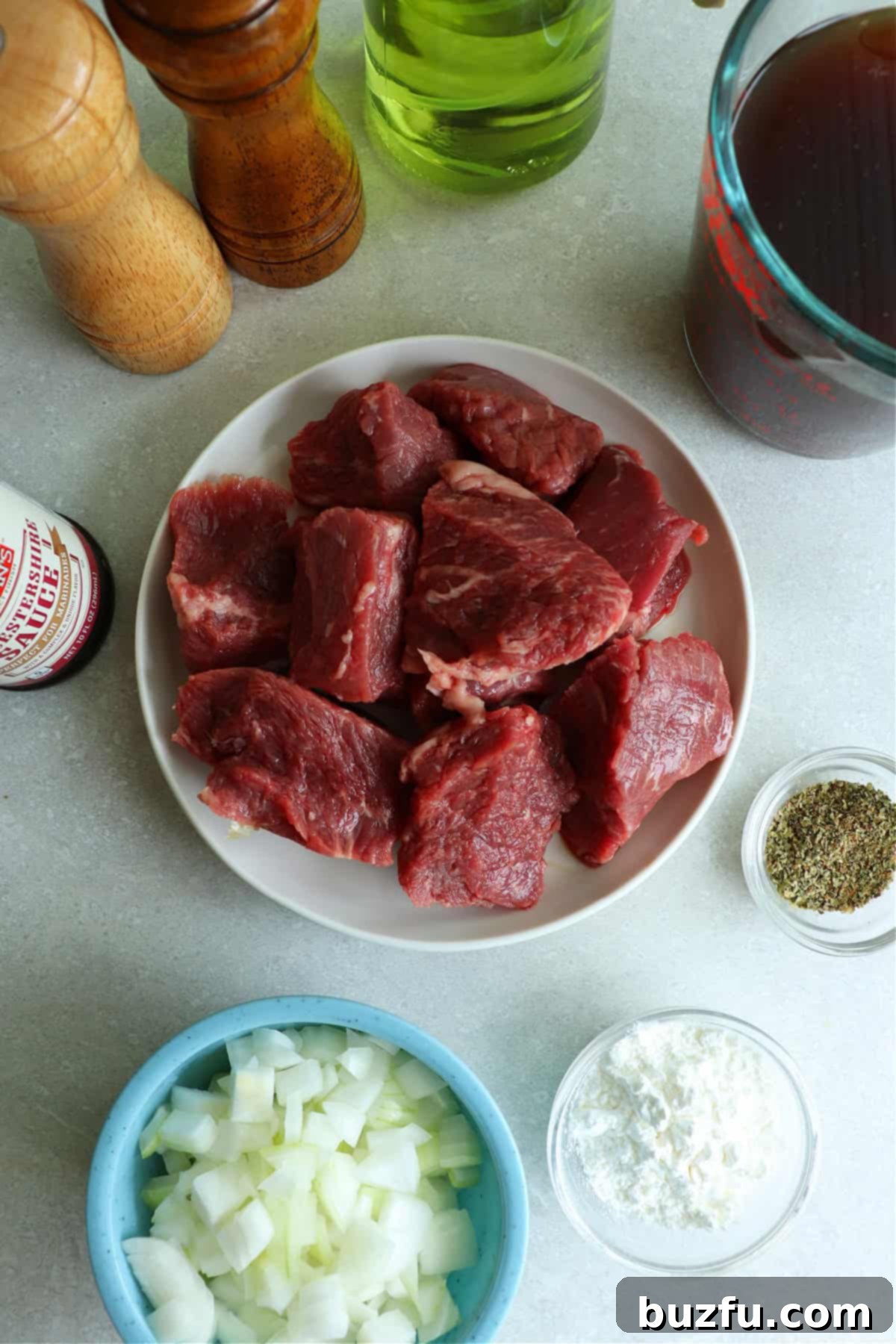 A vibrant flat lay photo showcasing the essential ingredients for Instant Pot Beef Tips: generously cut beef chunks, finely chopped yellow onion, a bowl of cornstarch ready for slurry, and a medley of dried seasonings including thyme and marjoram.