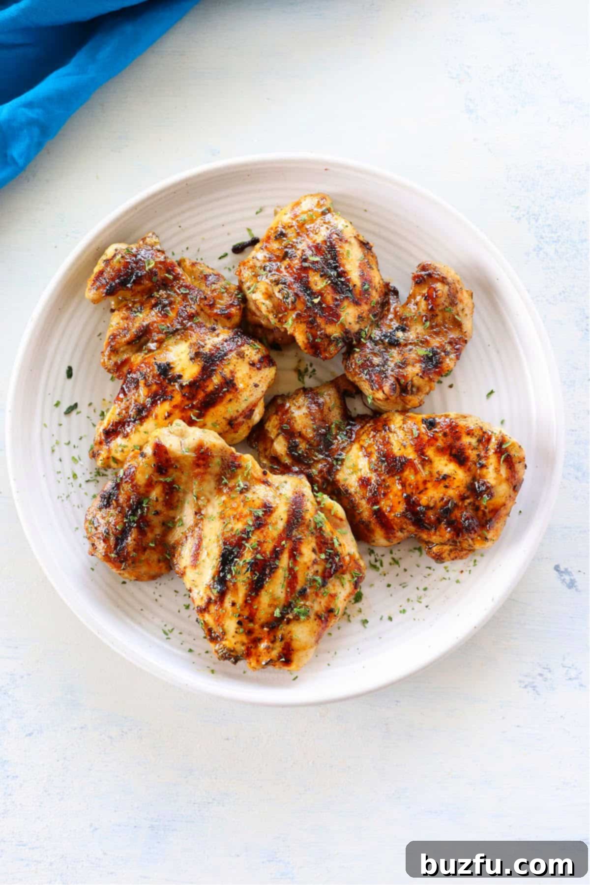 Week Six Meal Plan 3 Golden-brown grilled chicken thighs artfully arranged on a pristine white plate, garnished with fresh herbs, ready to be served.