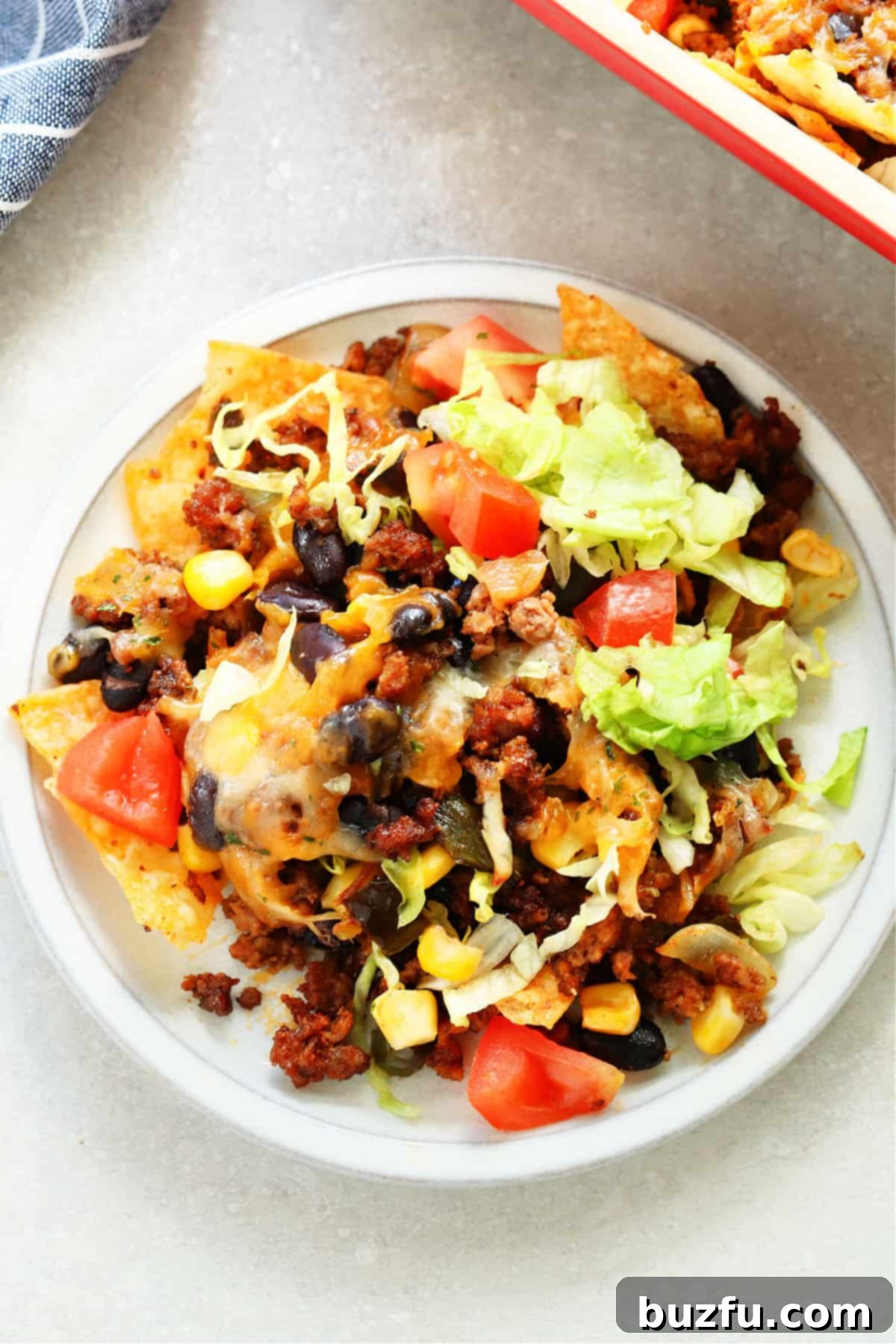 Week Six Meal Plan 4 A hearty and appealing taco casserole, served on a rustic gray plate, showing off its layers of seasoned meat, cheese, and crunchy toppings.