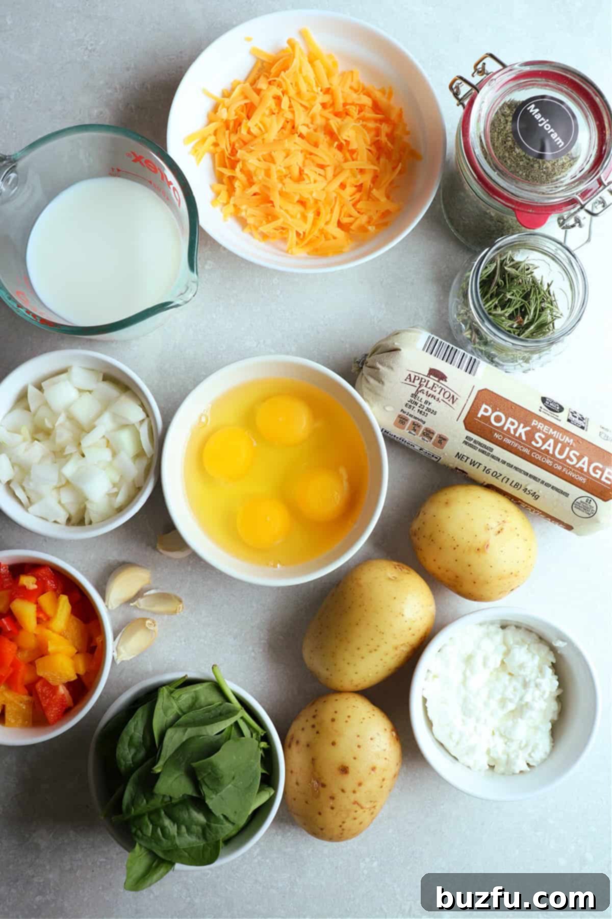 A photo of ingredients needed to make a quich with potato crust and ground sausage in the filling. All ingrdients are on a gray board, some in bowls.