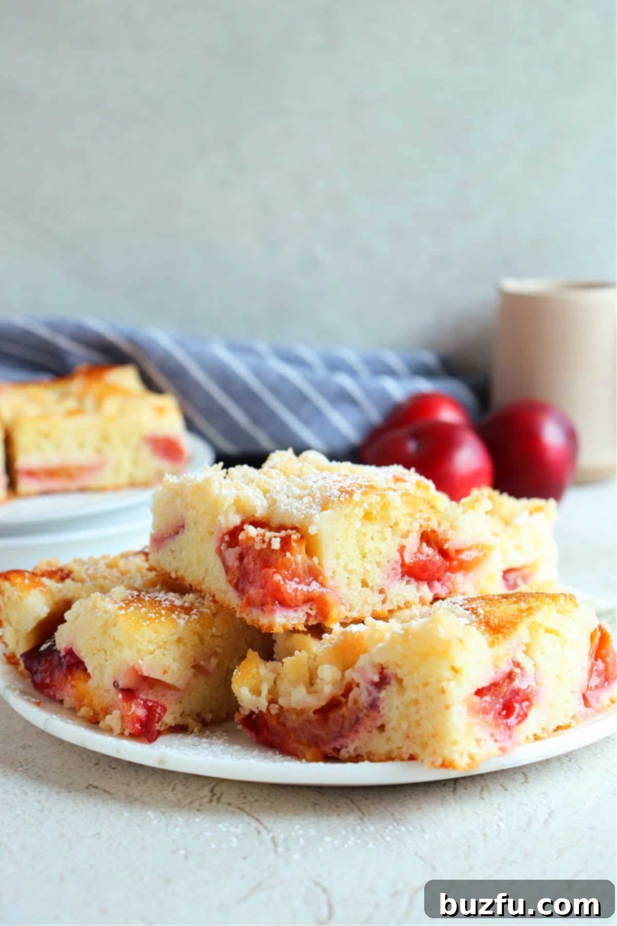 Three pieces of plum cake on a dessert plate, with fresh plums in the background.