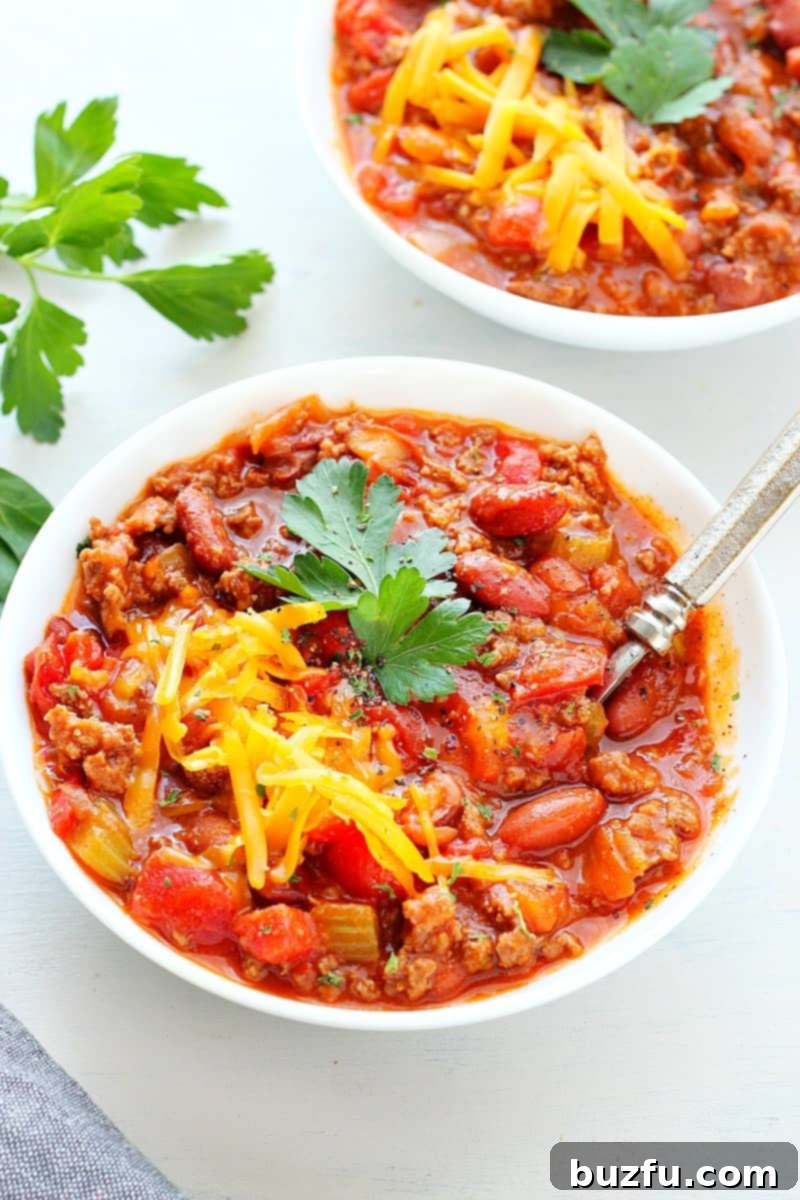 A close-up of a white bowl filled with hearty chili, generously topped with melted cheese, ready to be enjoyed.