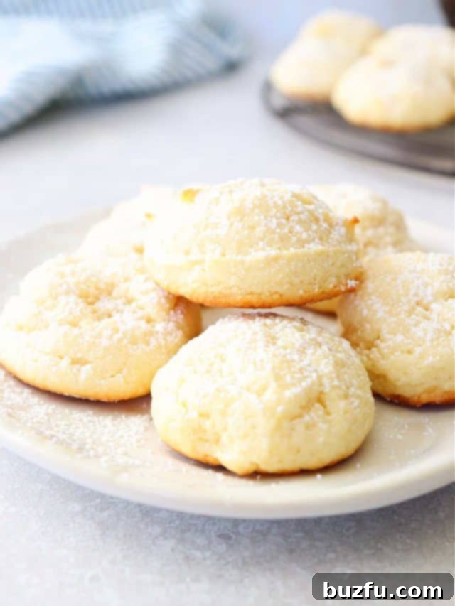 Close-up of a stack of soft and sweet cream cheese cookies, lightly dusted with powdered sugar.