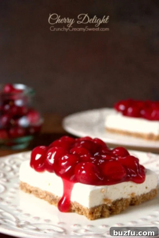 Side shot of a square slice of Cherry Delight dessert on a white plate, showcasing its distinct layers of crust, creamy filling, and cherry topping.