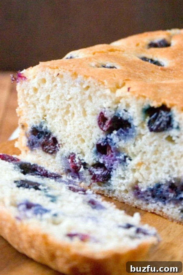 Sliced Blueberry Quick Bread on a wooden cutting board, showing fluffy interior and abundant blueberries.