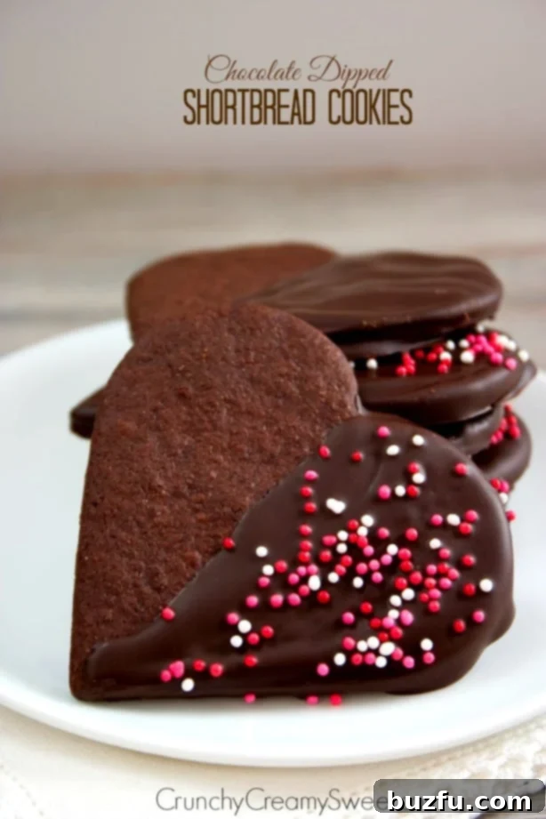 Side shot of chocolate dipped shortbread cookies in heart shapes, on white plate, decorated with pink sprinkles.