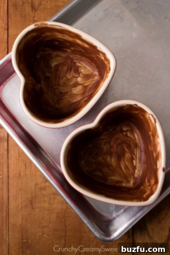 Overhead shot of heart shaped ramekins coated with cocoa mixture and set on baking sheet.