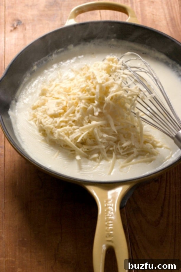 White sauce simmering with grated Pepper Jack cheese on top in a skillet, ready to be melted into a creamy sauce.