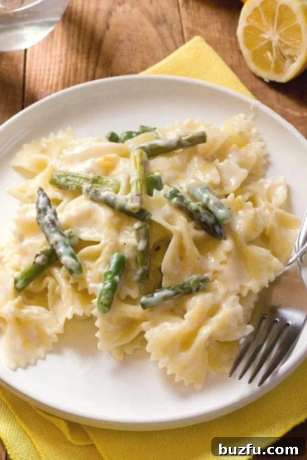A plate of Creamy Lemon Asparagus Pasta, garnished with fresh herbs and lemon wedges.