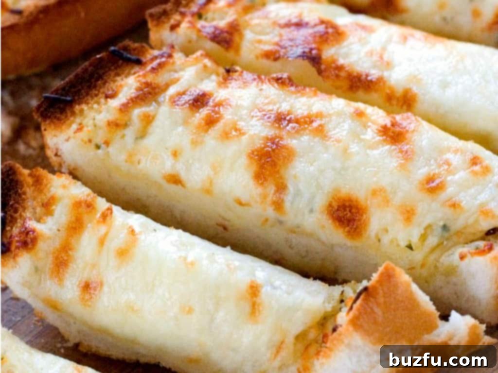Easy Cheesy Garlic Bread - perfect to go with pasta dishes or soups! Close up shot of sliced cheesy garlic bread on wooden cutting board, showcasing the melted cheese.