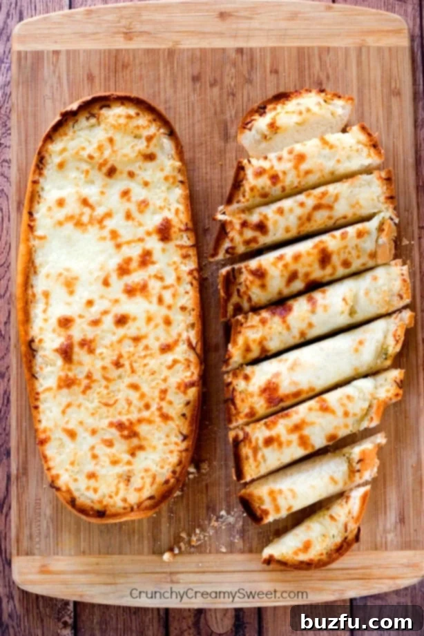 Easy Cheesy Garlic Bread - perfect to go with pasta dishes or soups! So easy and so good, you won't be able to stop eating it! Overhead shot of cheesy garlic bread on wooden cutting board, one half sliced and the second full, ready to be served.