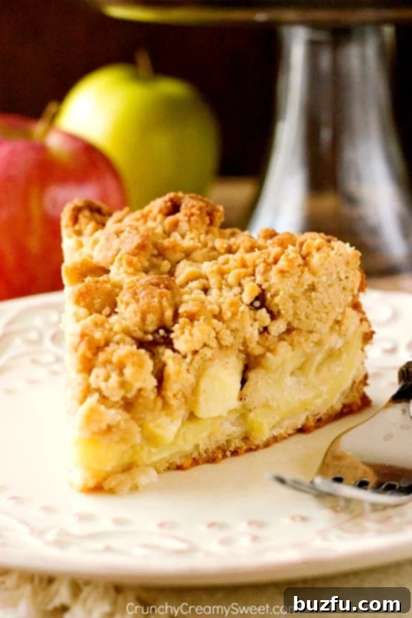 Delicious slice of Apple Crumb Cake on a white plate with a fork, showing layers of juicy apples and golden crumb topping.