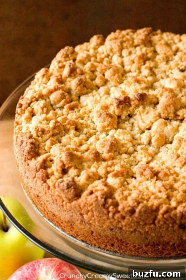 Side profile of a freshly baked Apple Crumb Cake on a glass cake stand, highlighting its rich layers and irresistible crumb texture.