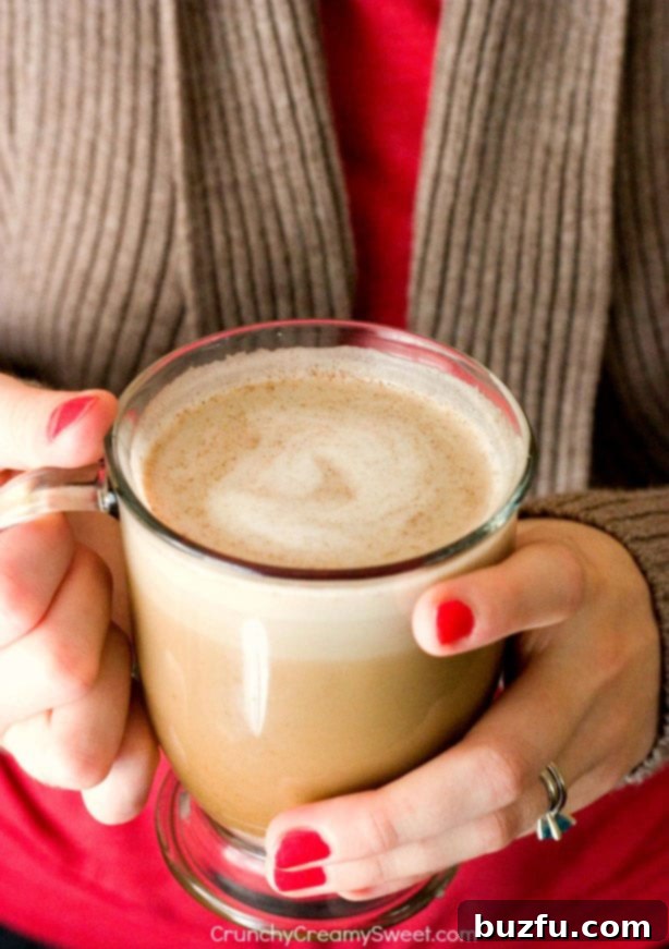 A woman's hands gently cupping a clear glass mug of pumpkin spice latte, showcasing its inviting warmth and creamy texture.
