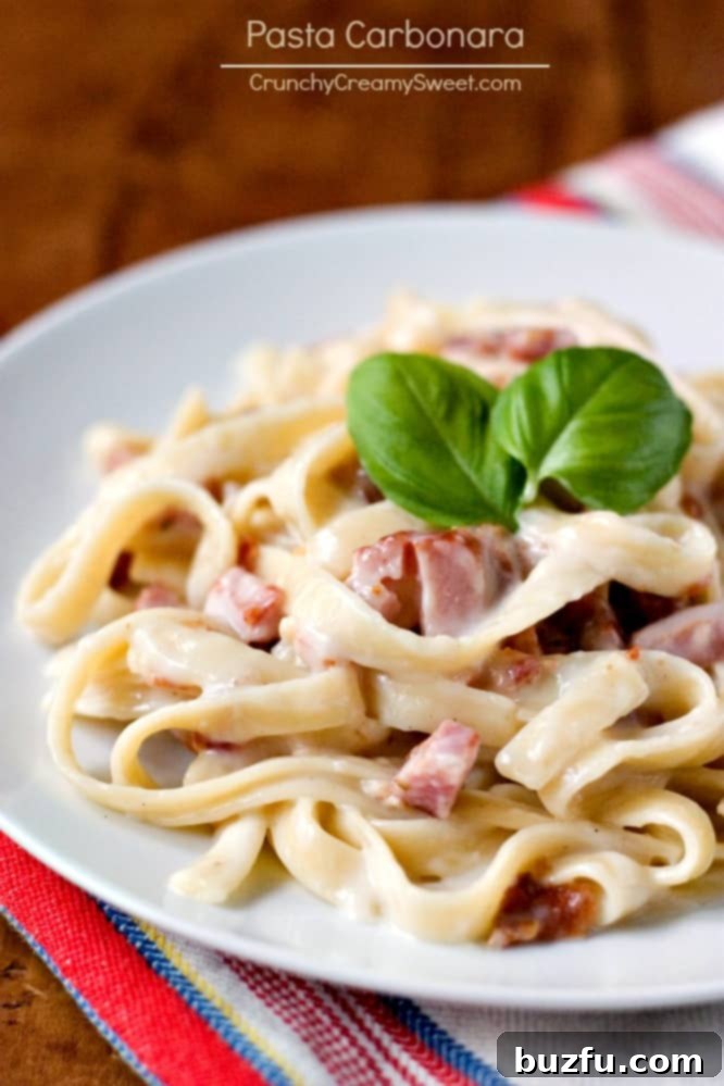 Side shot of pasta carbonara with ham on white plate.