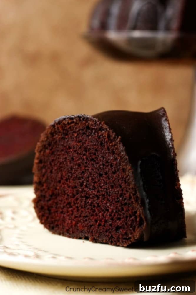 A perfect slice of The Best Chocolate Bundt Cake, showcasing its moist texture and rich chocolate flavor with a delicate glaze. Close up shot of a single, perfectly sliced piece of chocolate bundt cake on a white plate, revealing its moist crumb and rich color.