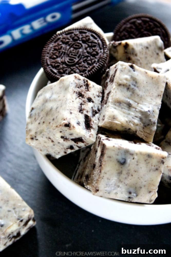 Easy Cookies and Cream Fudge for the Holidays Side view of perfectly cut Oreo fudge squares in a bowl, showing the rich white chocolate and dark cookie contrast.