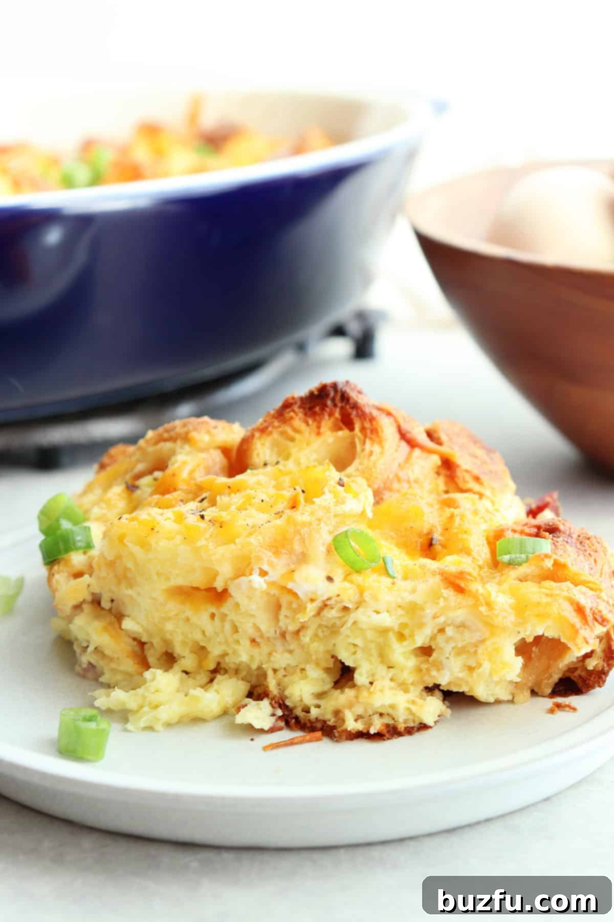 A serving of bread and egg casserole on a small plate with the casserole dish in the background.